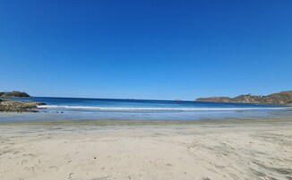 Una playa con cielos despejados, aguas tranquilas y afloramientos rocosos.