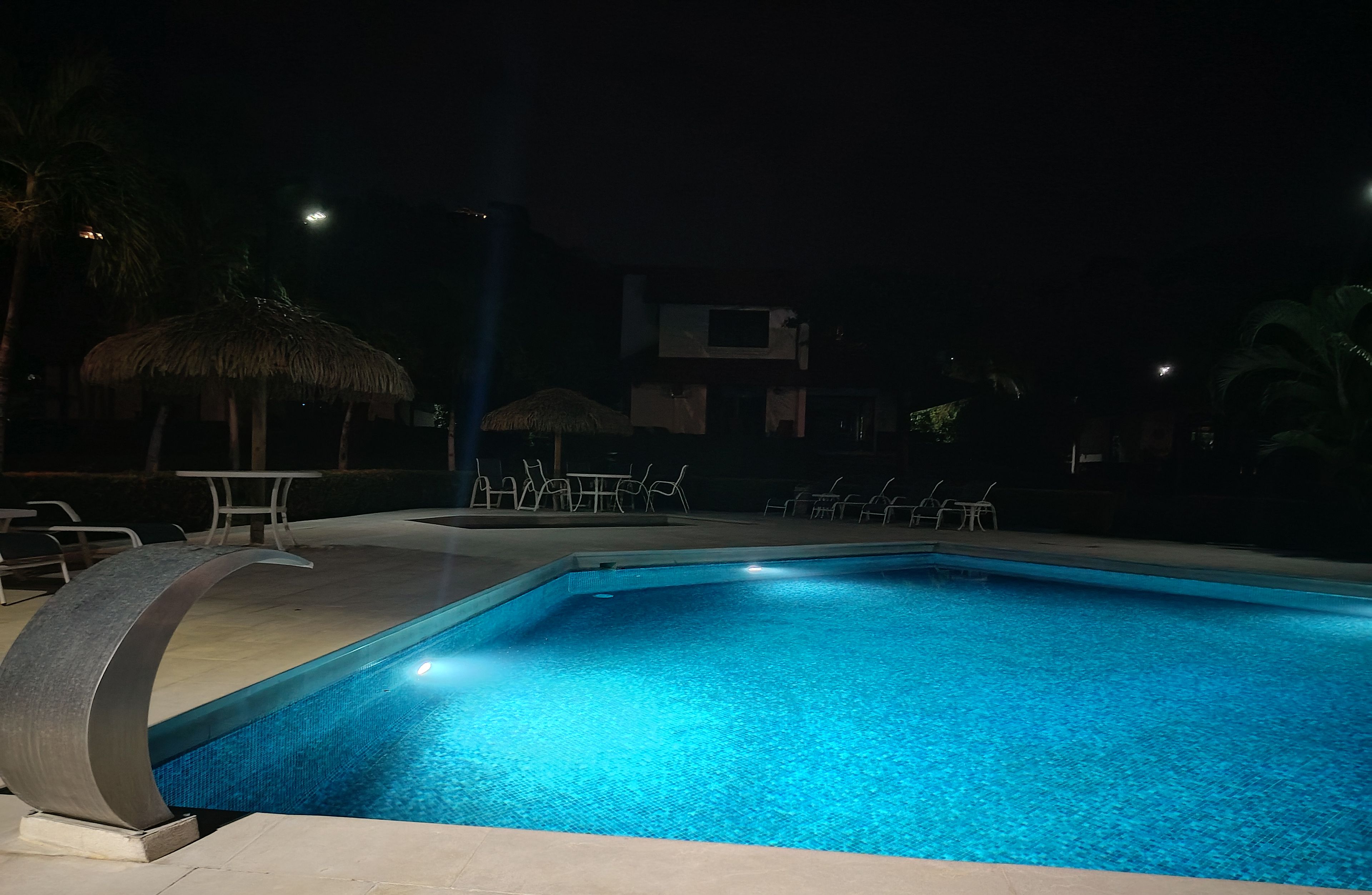 Una piscina con sillas de descanso y una sombrilla de paja.