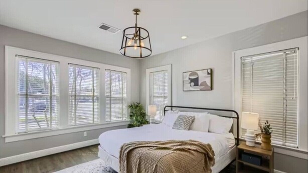 A bedroom with a large bed, white walls, and multiple windows with blinds.