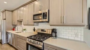 A modern kitchen with stainless steel appliances, white tiled backsplash, and light wood cabinetry.