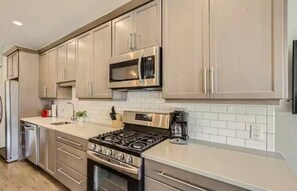 Una cocina moderna con electrodomésticos de acero inoxidable, salpicadero de azulejos blancos y armarios de madera clara.