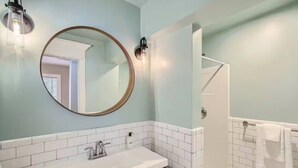 A bathroom with a round mirror, a sink, a shower, and a towel rack.