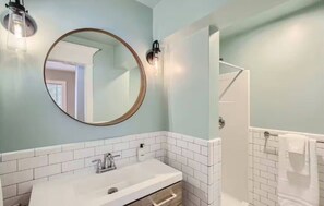 Un baño con espejo redondo, lavamanos, ducha y toallero.