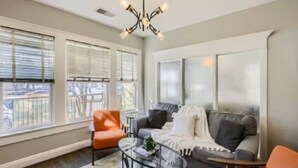 A living room with a sofa, armchairs, a coffee table, and large windows with blinds.