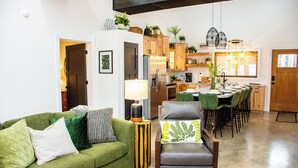 Un salon moderne avec un canapé vert, un fauteuil gris et un coin repas comprenant des chaises en bois, avec une cuisine en arrière-plan.