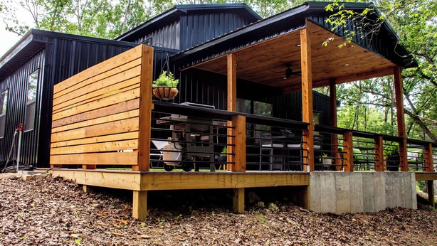 Une cabane moderne en bois, dotée d’une terrasse, de grandes fenêtres et d’un porche couvert.