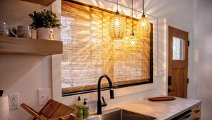 Une cuisine moderne dotée d’une grande fenêtre, d’un évier, de meubles en bois et d’un luminaire suspendu.