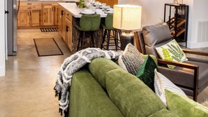 Une cuisine moderne avec des meubles en bois, un coin repas avec une chaise verte et un canapé vert dans le salon.