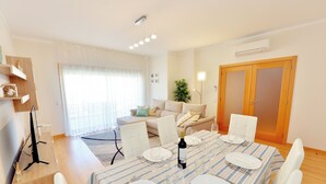 A dining area with a table set for four, a sofa, and a TV in the background. - FLORIPES LUXURY APARTMENT WITH POOL ON ROOFTOP (Olhão)