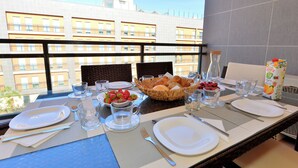 A dining table set with plates, cutlery, glasses, and a basket of bread and fruit on a balcony with a city view. - FLORIPES LUXURY APARTMENT WITH POOL ON ROOFTOP (Olhão)