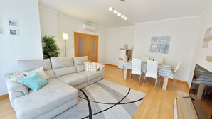 A modern living room with a sofa, a dining table with chairs, and a TV. - FLORIPES LUXURY APARTMENT WITH POOL ON ROOFTOP (Olhão)