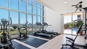 A gym with treadmills, elliptical machines, and weight equipment, large windows, and a view of a swimming pool. - Beachy Malibu Loft - Pool / Tennis / Gym (Malibu)