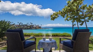 Une terrasse dotée de chaises et d’une table en osier, offrant une vue imprenable sur la côte, avec des maisons et l’océan.