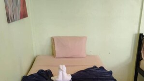 Una cama con colchón color beige, almohada rosa y un objeto decorativo blanco sobre la cama.