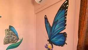 Een slaapkamer met een bed, een wanddecoratie van vlinders, een raam met gordijnen en een bakstenen muur.