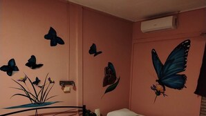 Een slaapkamer met twee bedden, een plafondventilator en vlinderdecoratie aan de muur.