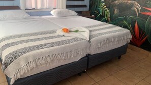 Una cama con ropa de cama estampada, un cojín decorativo y un mural tropical de fondo.