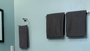 Une salle de bain équipée d’un lavabo, de deux serviettes, de toilettes et d’une petite table en bois sur laquelle est posé un rouleau de papier toilette.