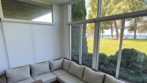 Eine Sitzecke mit gepolsterten Bänken und einem Holztisch, große Fenster mit Blick auf eine Rasenfläche und Bäume.