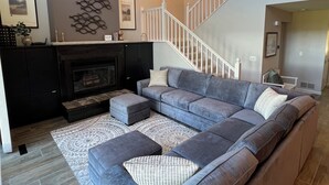 Ein Wohnzimmer mit Ecksofa, Poufs, Kamin und Treppe.
