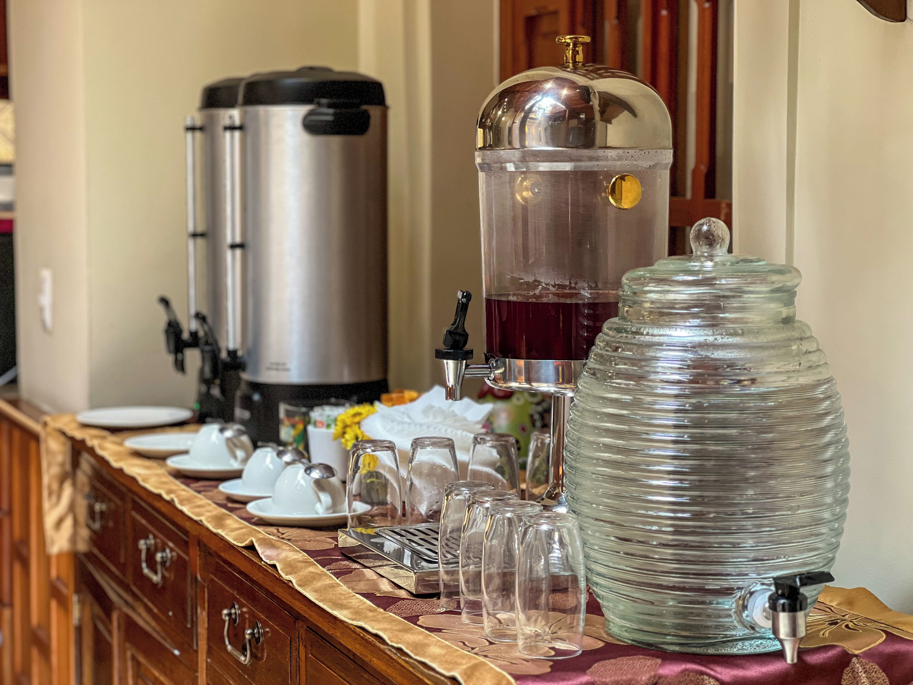 Un buffet avec un coin café, un distributeur d’eau et un grand récipient en verre, probablement destiné à contenir de la glace ou de l’eau.