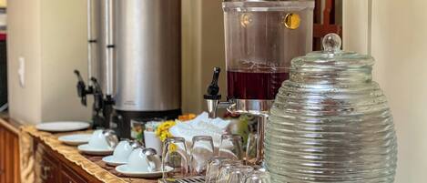 A buffet setup with a coffee station, a water dispenser, and a large glass container, likely for ice or water.