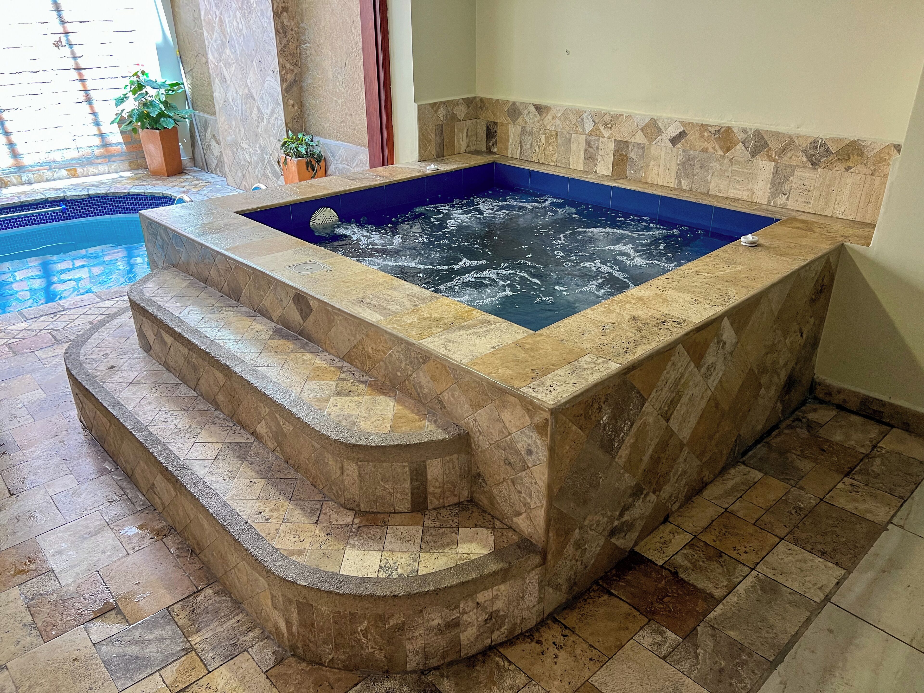 Ein Whirlpool mit Steinfassade und blauer Innenausstattung, umgeben von einer Steinfläche und Stufen, die zu ihm hinaufführen.