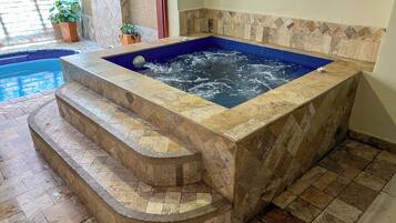 Ein Whirlpool mit Steinfassade und blauer Innenausstattung, umgeben von einer Steinfläche und Stufen, die zu ihm hinaufführen.