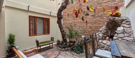 A courtyard with a brick wall, a wooden bench, a table, and chairs.