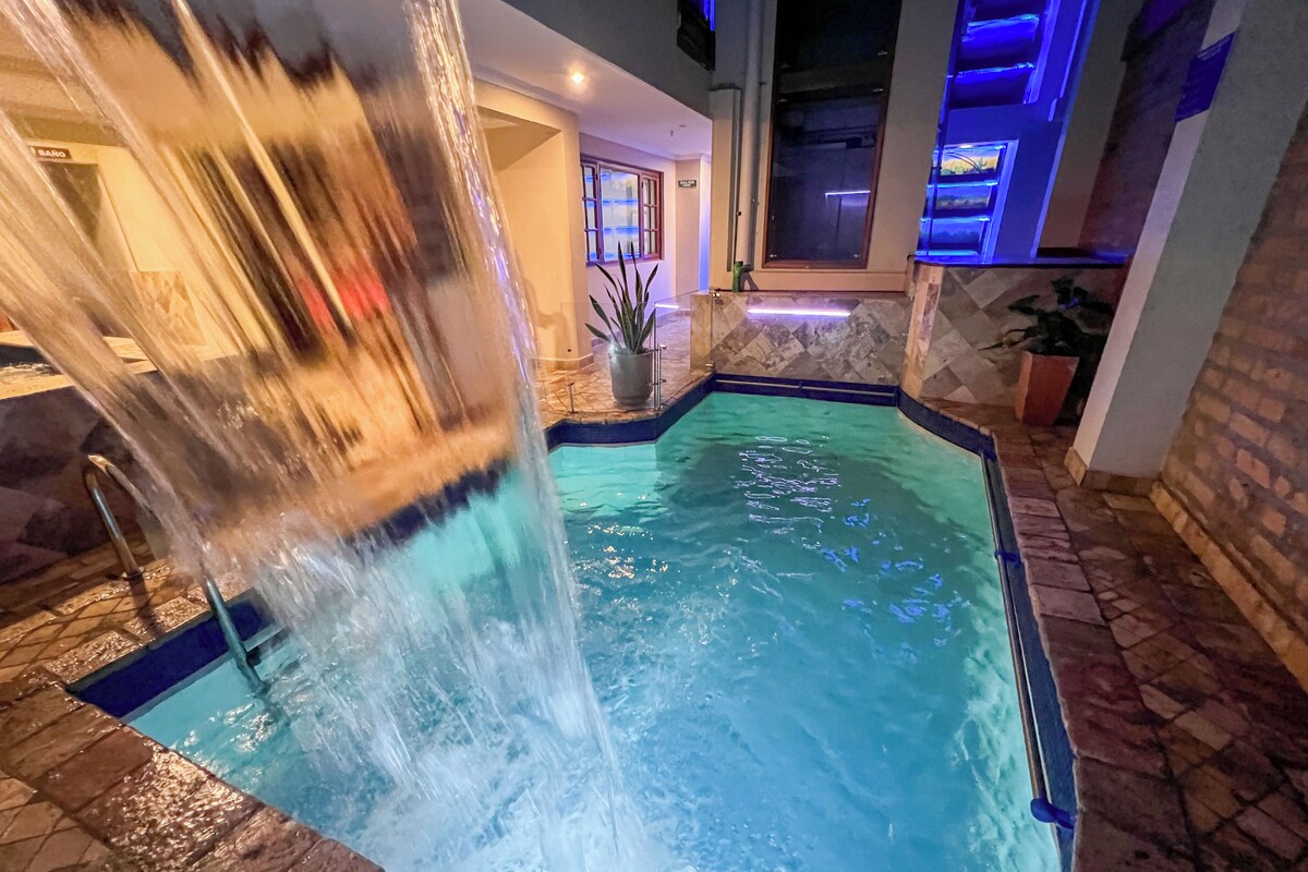 Ein Pool mit Wasserfall, umgeben von Steinplatten und einer Topfpflanze.
