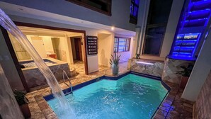 An indoor swimming pool with a waterfall feature, stone-tiled flooring, and a sign indicating pool rules. - Hotel Boutique Magdalena By Chat Noir (Cuenca)