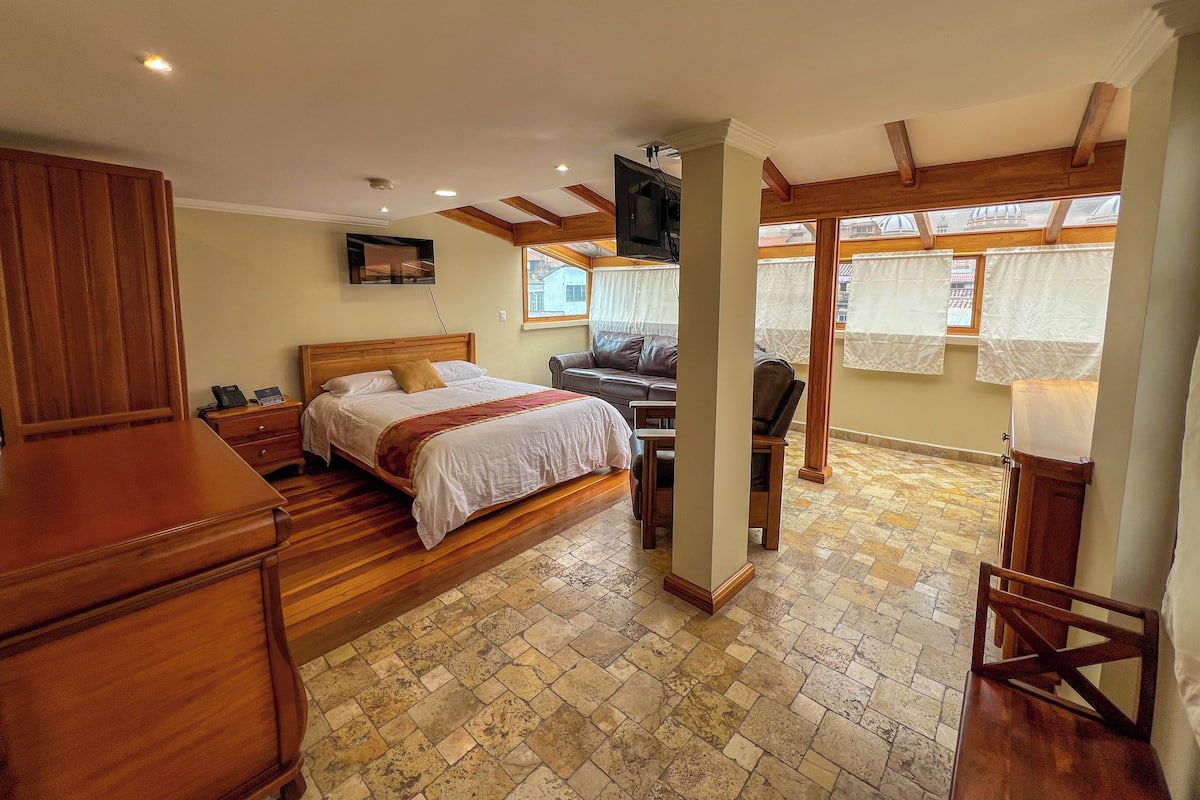 A bedroom with a bed, wooden furniture, a TV, and a view through the window.