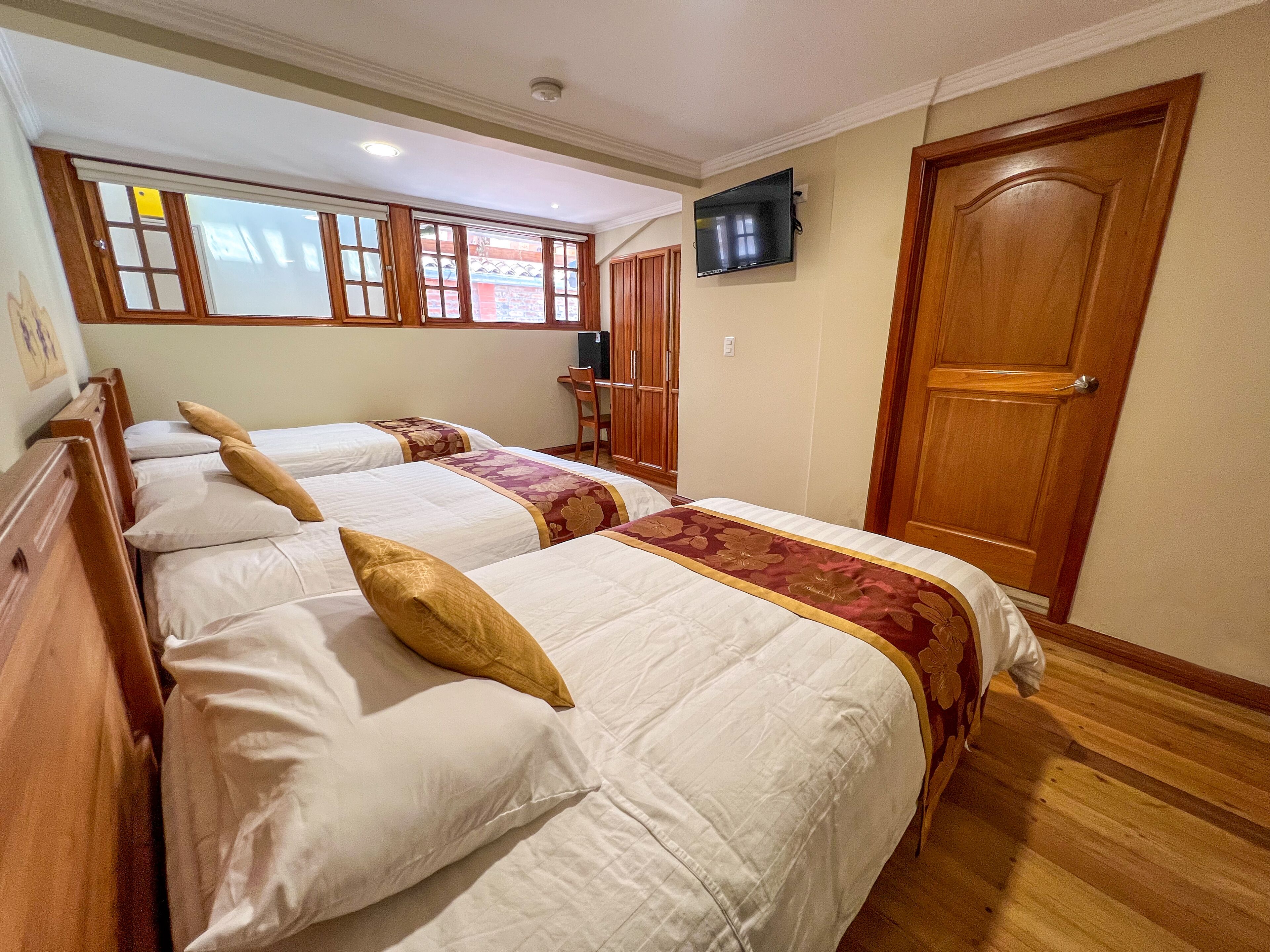 Een hotelkamer met drie bedden, een aan de muur bevestigde televisie en een houten deur.