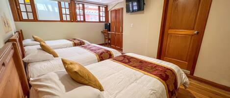 Une chambre d’hôtel avec trois lits, un téléviseur fixé au mur et une porte en bois.