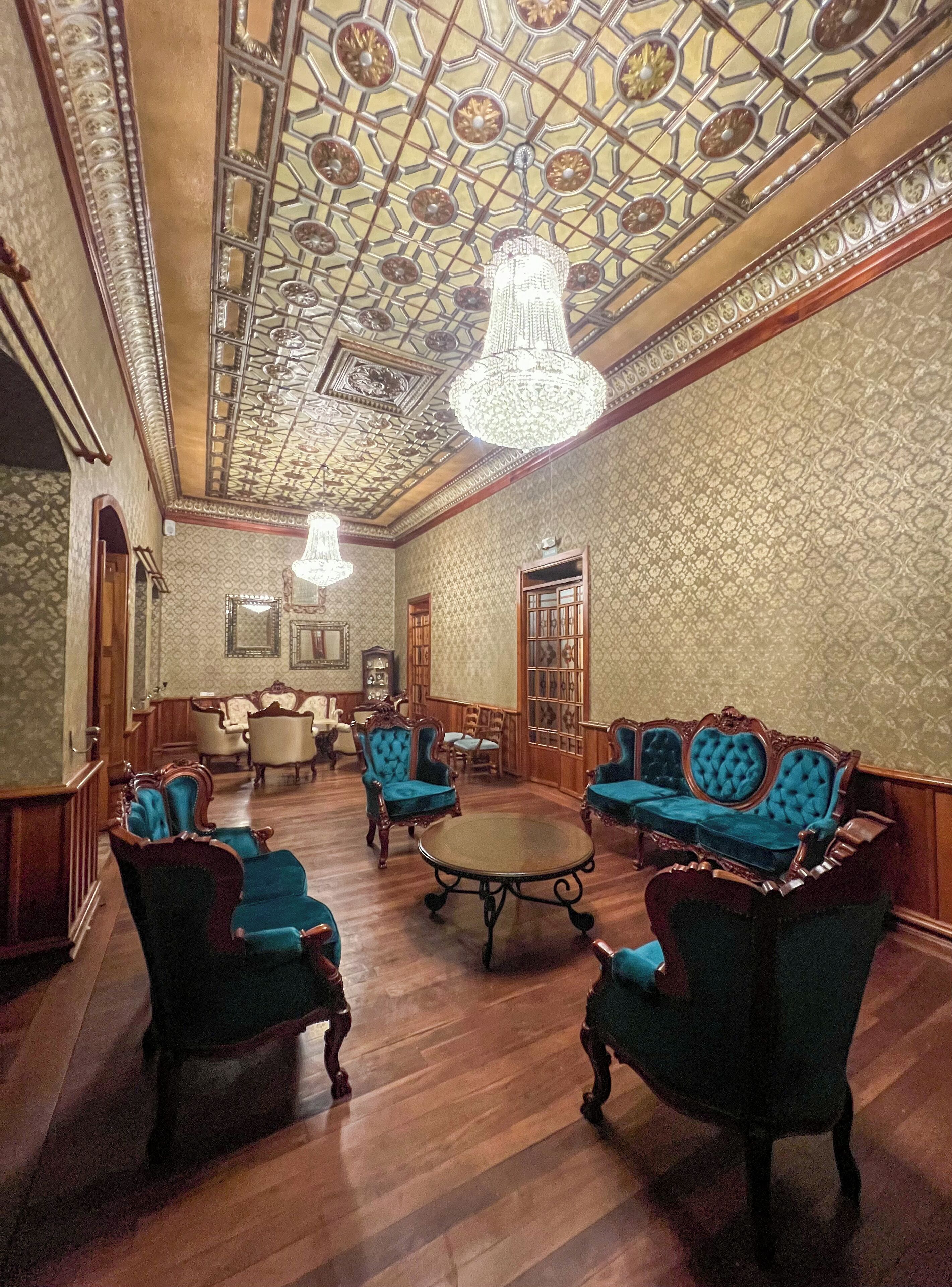 A room with ornate ceiling, chandeliers, and vintage furniture.