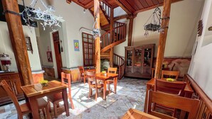 A spacious dining area with wooden tables and chairs, a staircase, and a cabinet with glass doors. - Hotel Boutique Magdalena By Chat Noir (Cuenca)