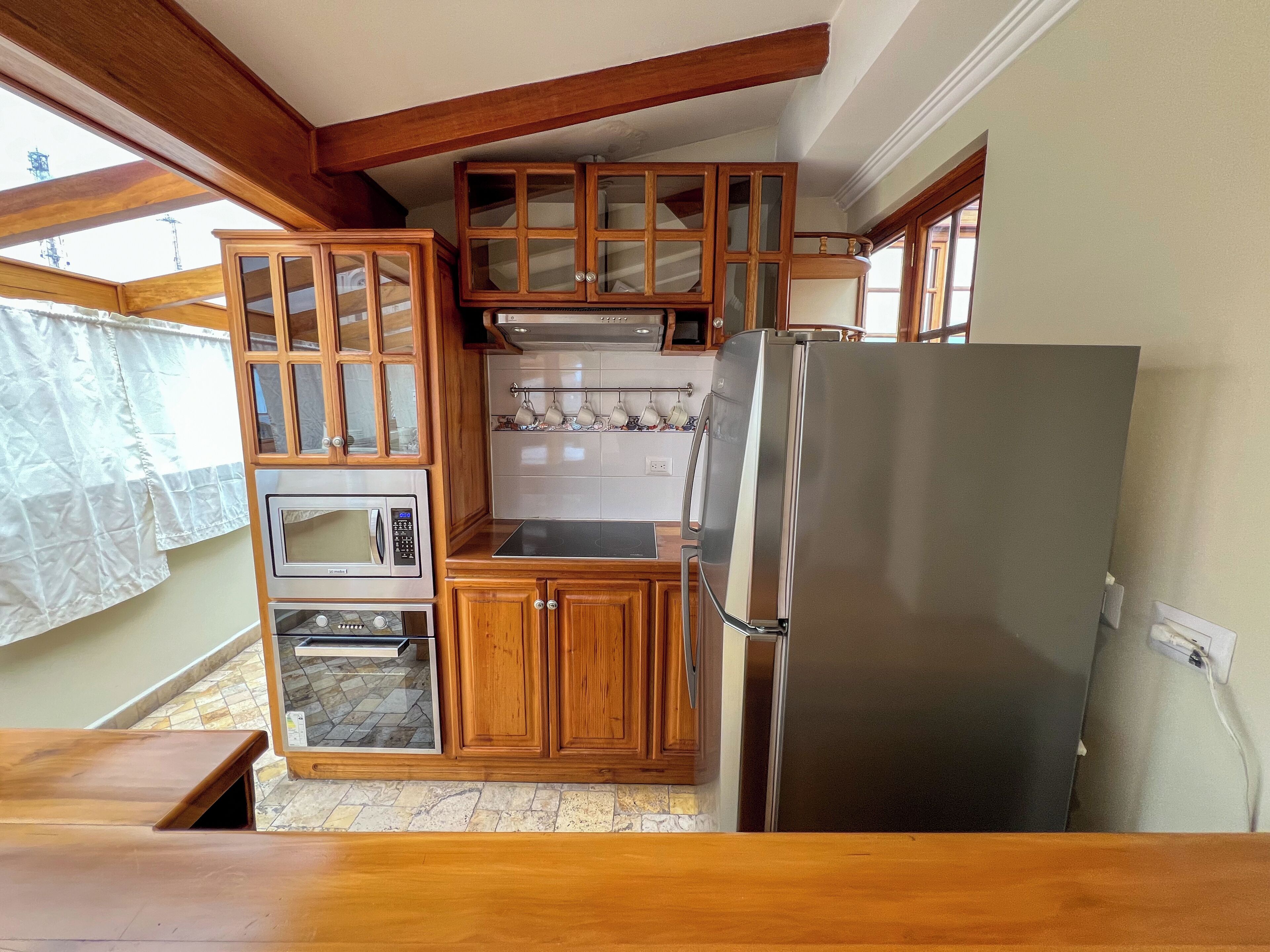 A compact kitchen with wooden cabinets, a stainless steel refrigerator, a microwave, and a built-in oven.