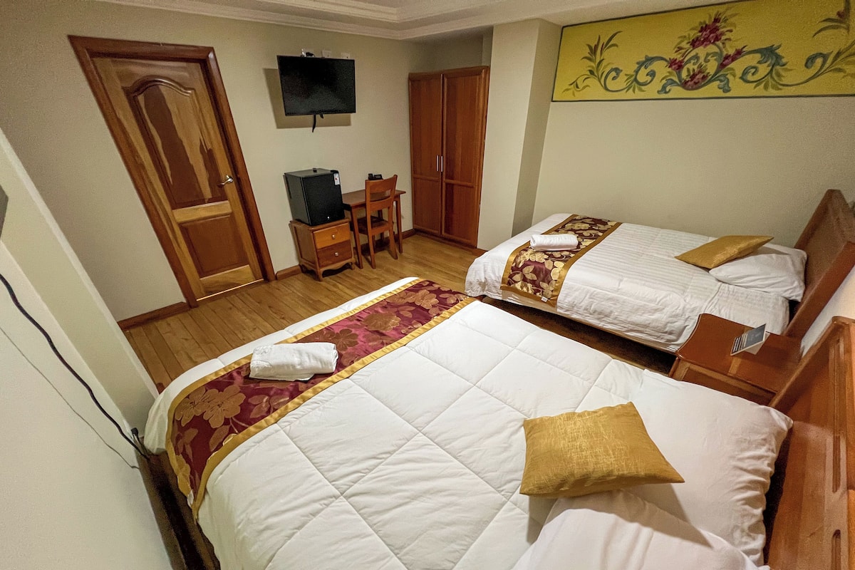 A hotel room with two beds, a TV, a desk with a computer, and a wardrobe.
