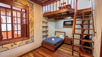 A bedroom with a wooden bunk bed, a single bed, a wooden ladder, a TV, and a window with decorative shutters.