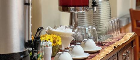 Un buffet avec une machine à café, un distributeur d’eau et de la verrerie empilée sur une table en bois.