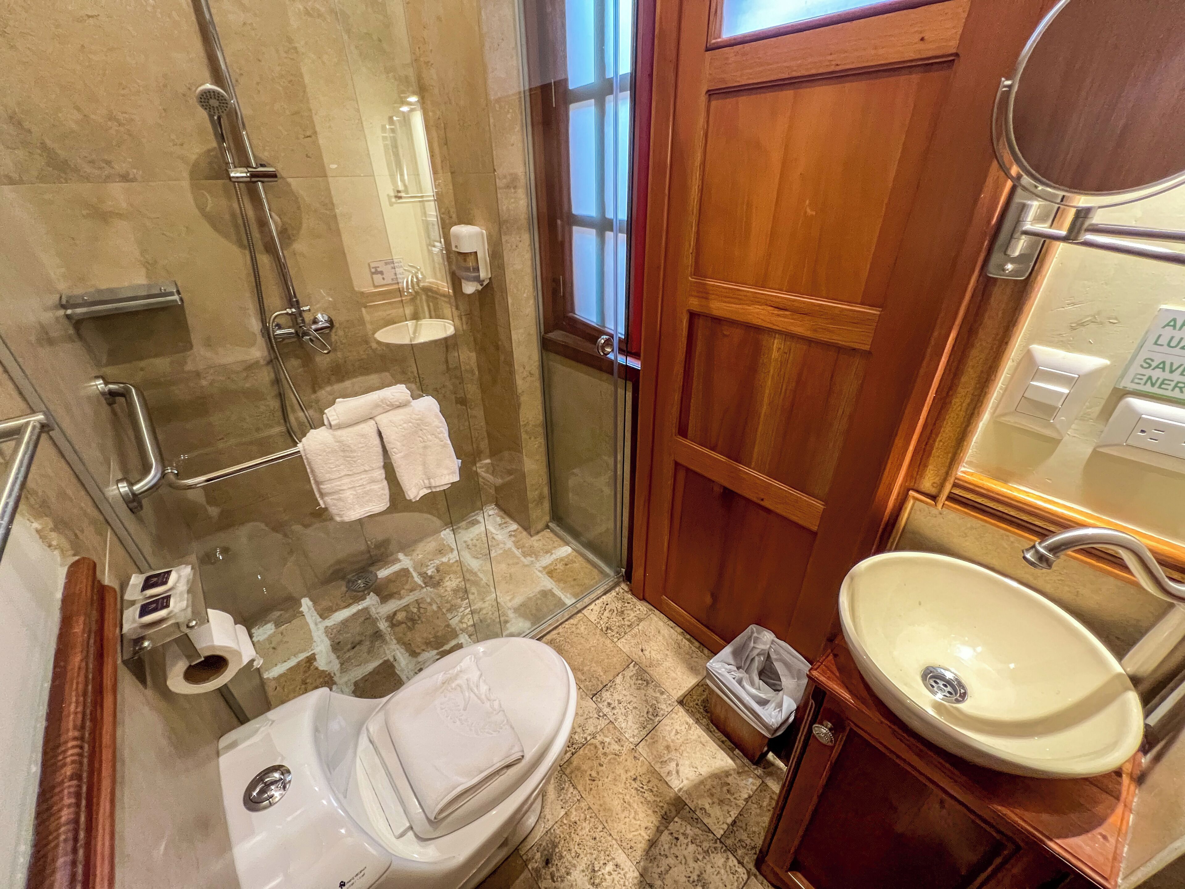 Un baño con ducha de vidrio, inodoro, lavamanos y puerta de madera.