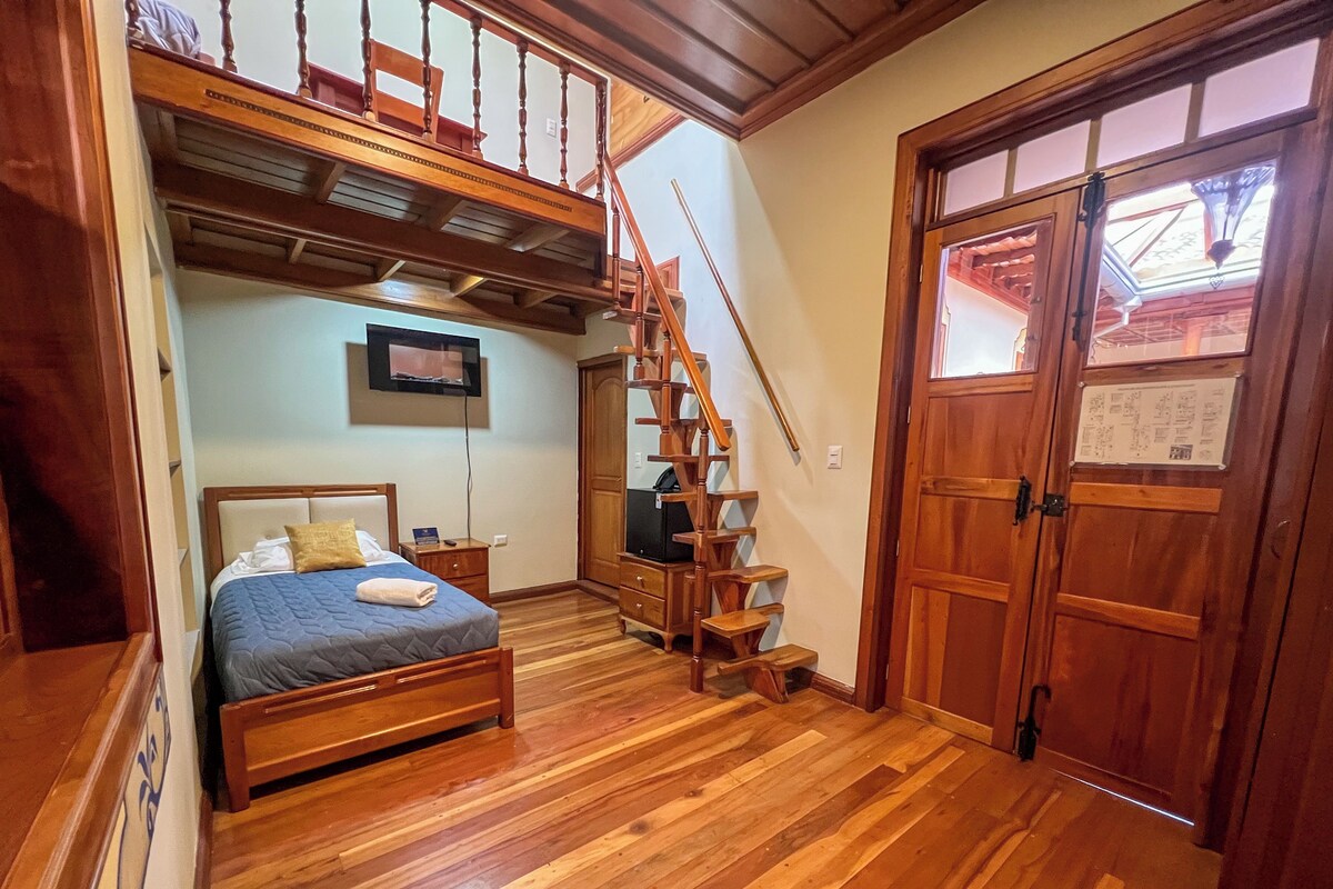 Une chambre à coucher avec un lit en bois, une télévision, un escalier et une porte avec une fenêtre.