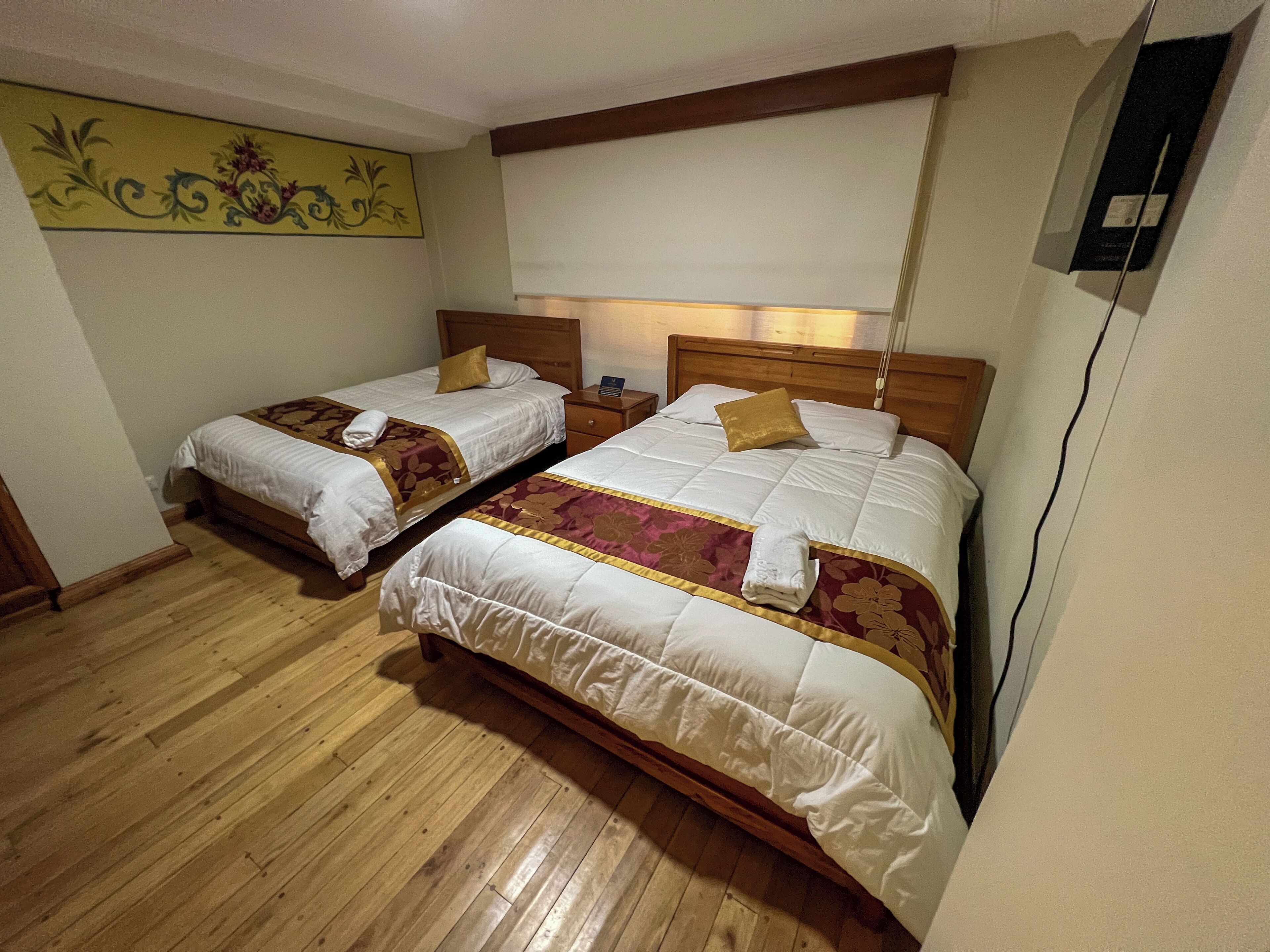 A hotel room with two single beds, wooden flooring, and a decorative wall piece.