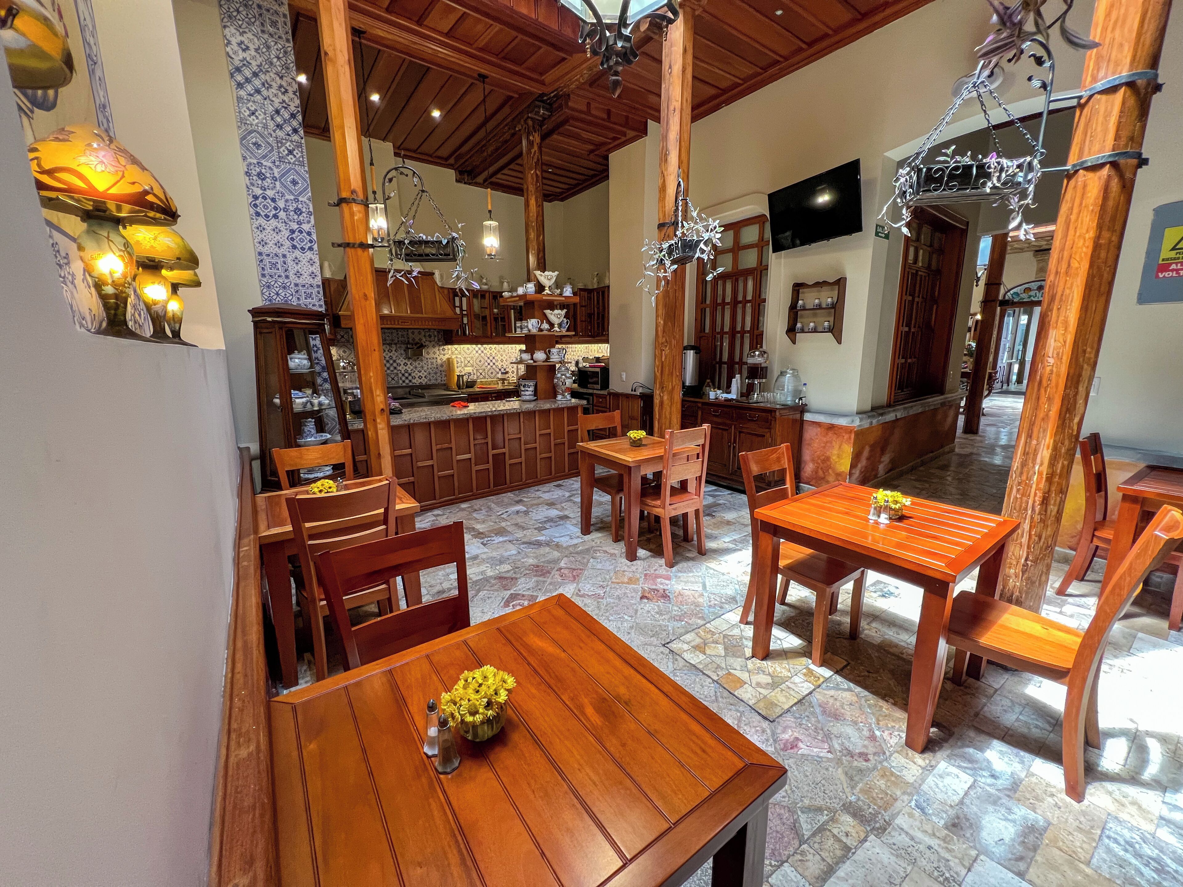 Un comedor amplio con mesas y sillas de madera, una cocina al fondo y suelo de baldosas.
