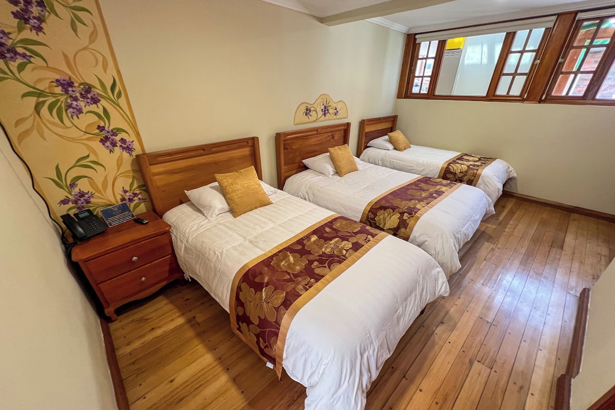 A hotel room with two wooden beds, a wooden nightstand with a phone, and a floral wallpaper.