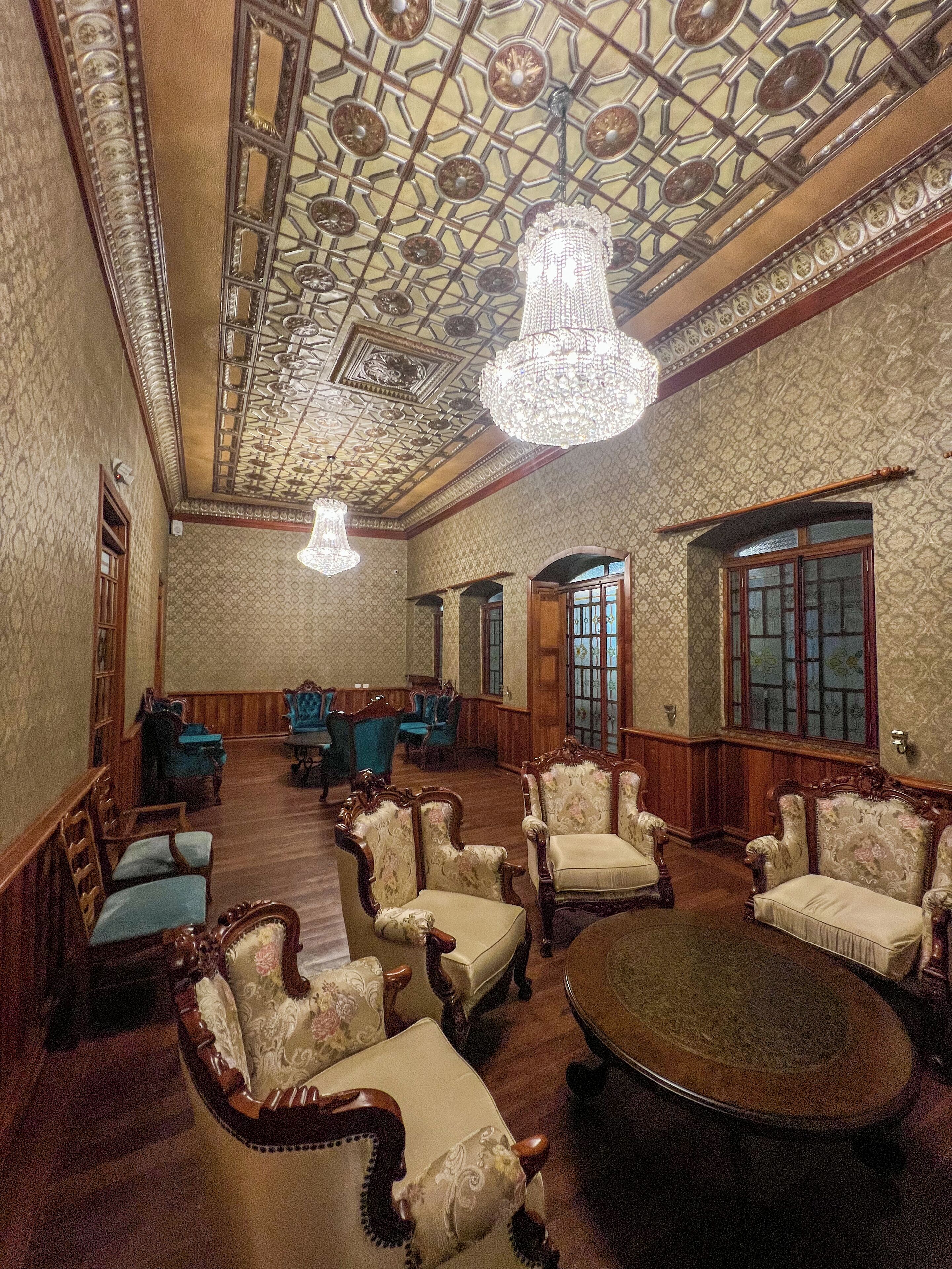 A spacious room with ornate ceiling, chandeliers, and classic furniture.