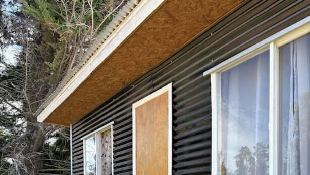 Una cabaña con terraza de madera, una puerta y dos ventanas.