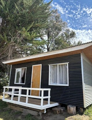 Eine kleine, eingeschossige Holzhütte mit einer Holzterrasse und einem großen Fenster.