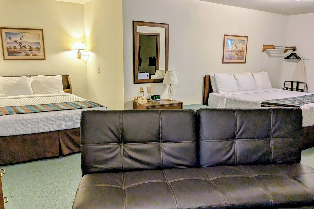 A hotel room with two beds, a sofa, and a nightstand with a lamp and phone.