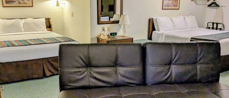 A hotel room with two beds, a sofa, and a nightstand with a lamp and phone.